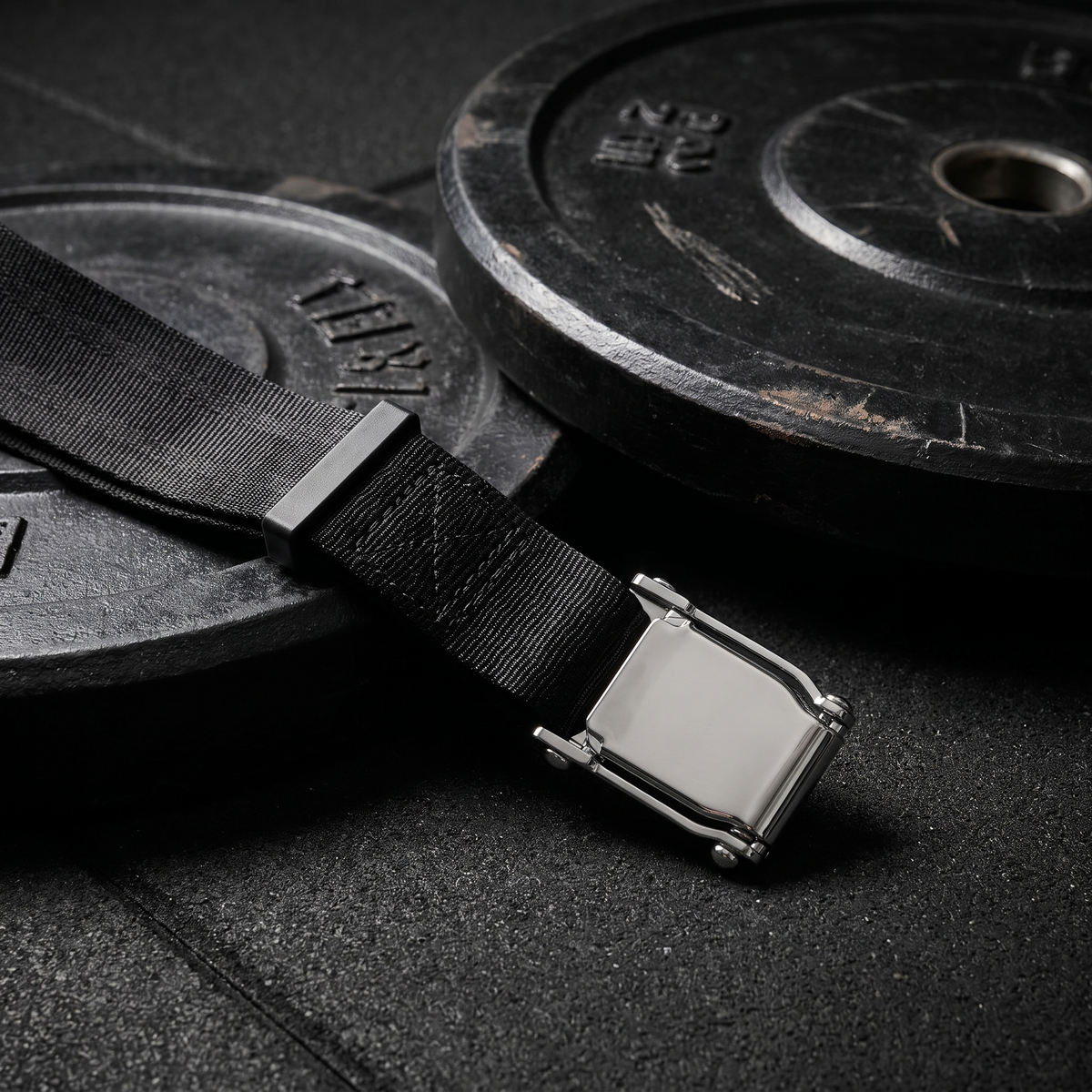 Nordic curl strap on a gym floor beside a weight plate