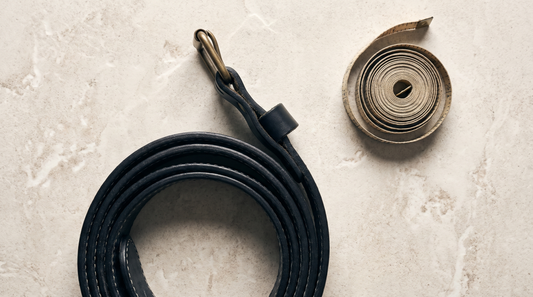A black leather weightlifting belt laid flat beside a tape measure