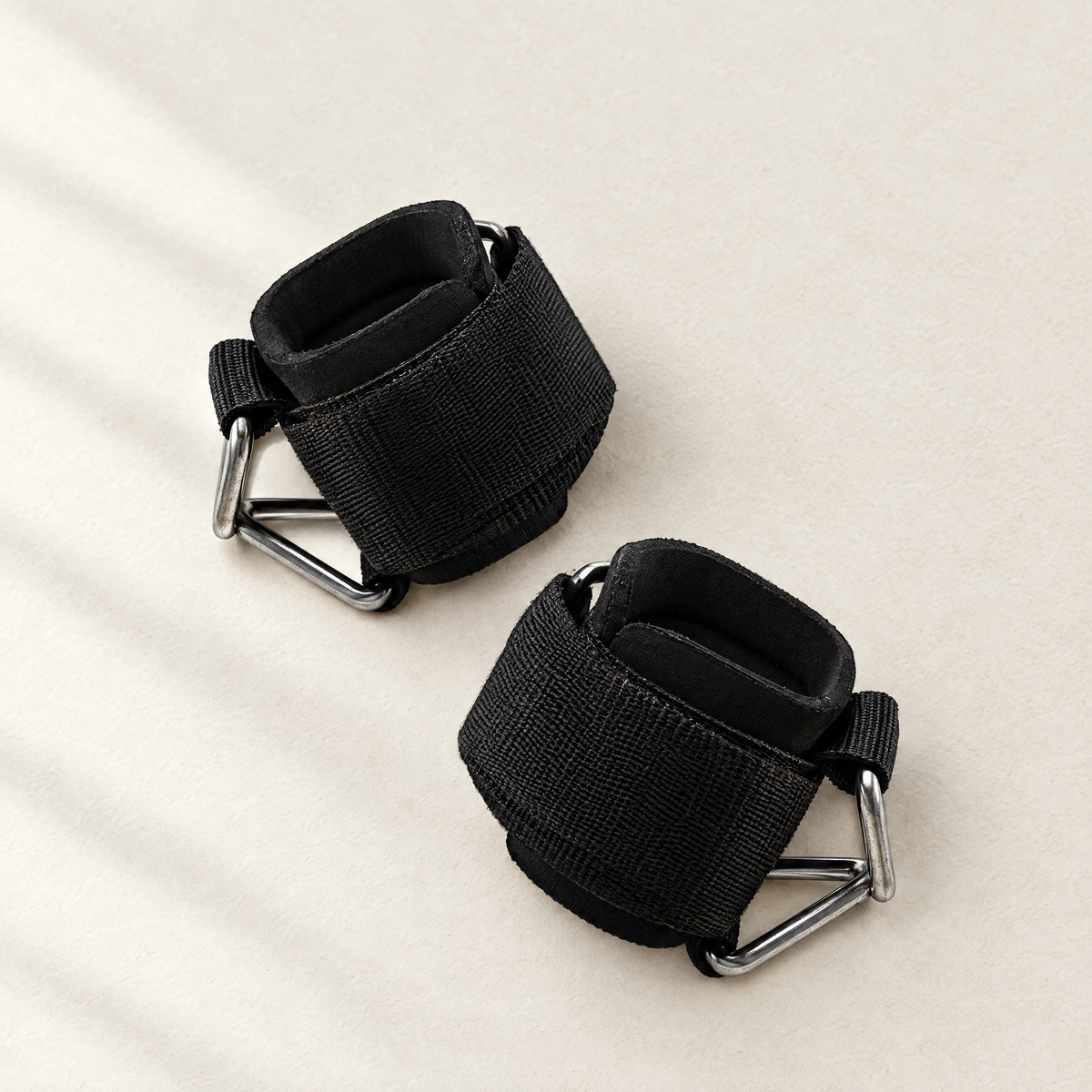 Pair of padded D-ring cable cuffs on a bone background