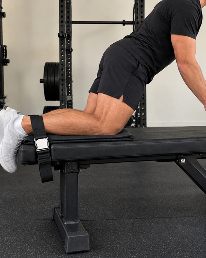 Nordic curl strap cinched over ankles on a flat bench, rear view
