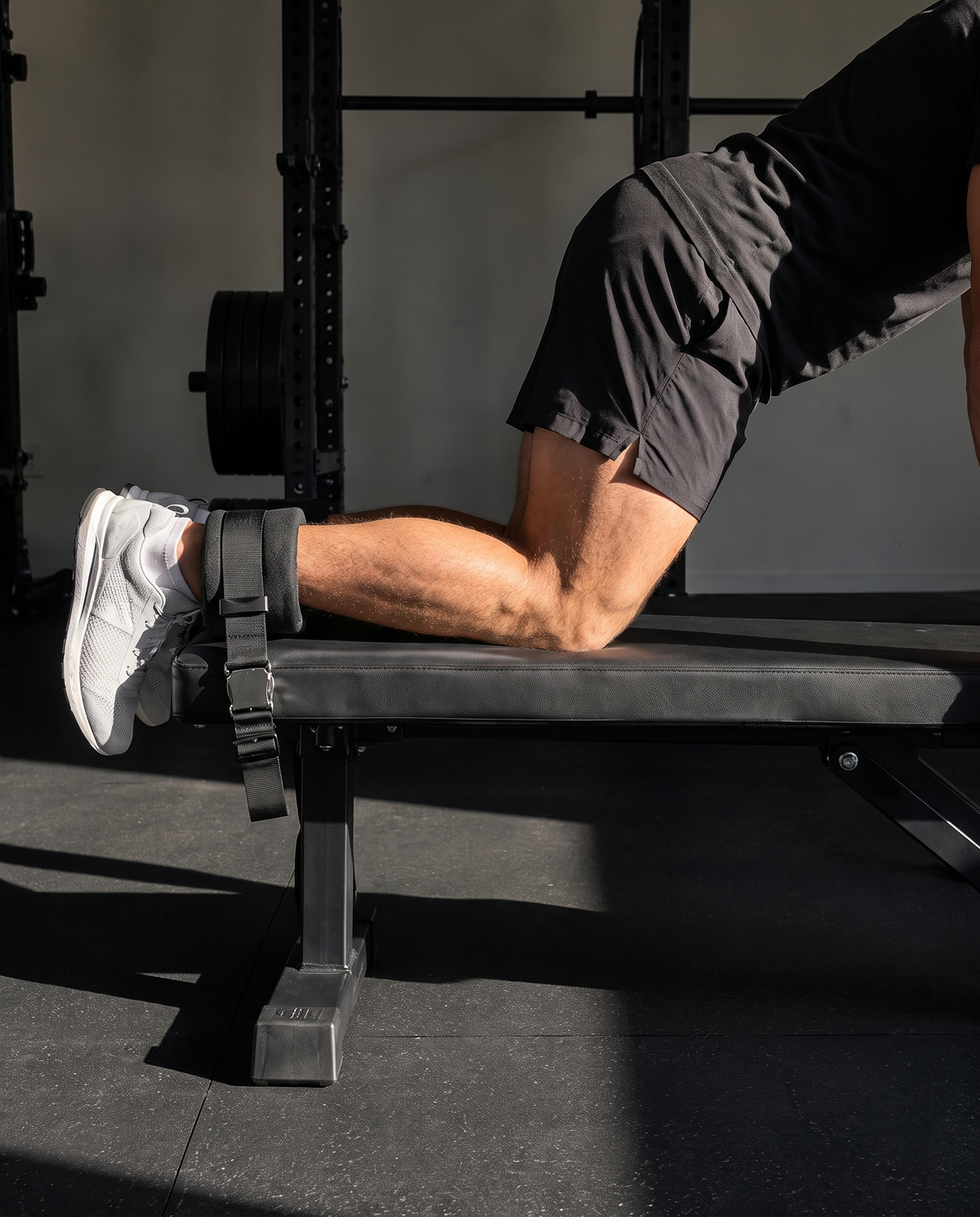 Nordic curl strap anchored under a bench with ankles hooked in mid-curl