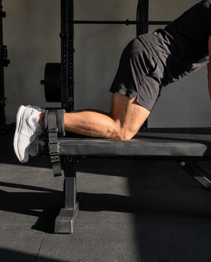 Nordic curl strap anchored under a bench with ankles hooked in mid-curl