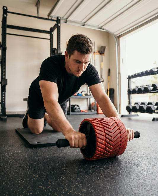 Lifter mid rollout on a wide red ab roller wheel on a knee mat in a garage gym